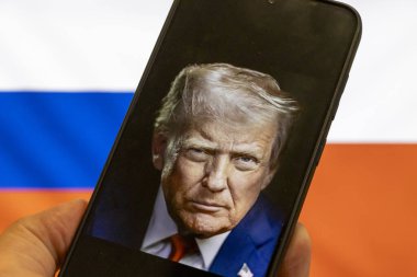Warsaw Poland - September 17 2025: A person holding a smartphone displaying a portrait of Donald Trump against flags symbolizing the Ukraine war reflecting political tensions.