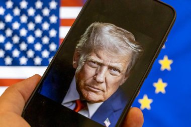 Warsaw Poland - September 17 2025: A close-up of a smartphone displaying Donald Trump against the backdrop of American and European flags symbolizing political tension and global relations.