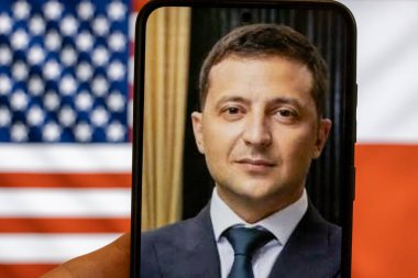 Warsaw Poland - September 17 2025: Close-up of Volodymyr Zelensky on smartphone screen emphasizing his leadership during Ukraine war with American and Polish flags in background.