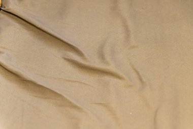 Tarafsız kahverengi bir gölgede, arka plan tasarımı veya tekstil ile ilgili projeler için uygun doku ve derinliği vurgulayan kırışık bir kumaş yüzeyinin yakın çekimi.