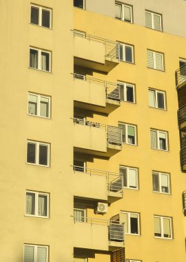 Şehir mimarisini ve metropoliten bir alanda çağdaş tasarımı temsil eden sarı cephe ve balkonları gösteren modern bir konut binasının yakın görüntüsü.