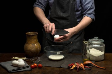 Erkek eller hamur yapmak için bir yumurtayı cam kaseye kırıyorlar. siyah arkaplan