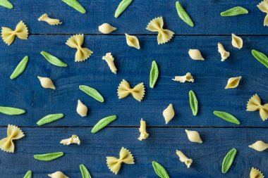 Mavi arka planda farklı şekillerde ham makarna. en üstteki görünüm