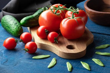 Ahşap tahtada domates ve salatalık, mavi arka planda çiğ makarna.