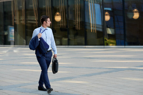 Tired young businessman with case going after work in hot weather  