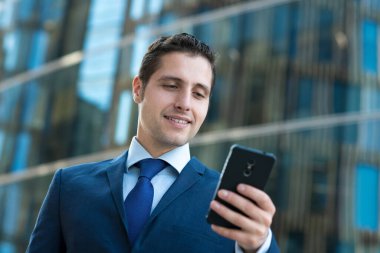 Mutlu genç işadamı camdan binadan telefonla mesaj yolluyor.