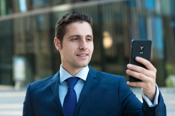 Szczęśliwy Młody Biznesmen Smsuje Wiadomość Przez Telefon Zewnątrz Szklanego Budynku — Zdjęcie stockowe