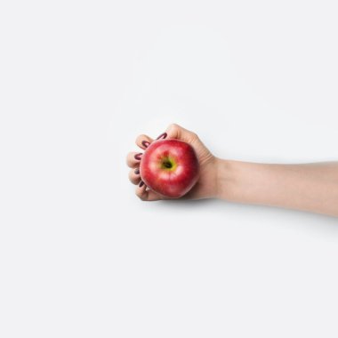 Female hand with red nails hold red apple on grey background clipart