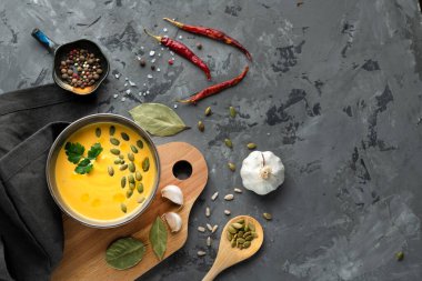 Çekirdekli kabak çorbası, maydanoz, sarımsak, defne yaprağı, baharatlar, peçete ve kaşıkla gri masada biber, üst manzara. Metin için boşluk