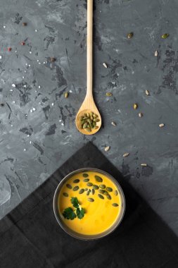 Gri zemin üzerinde kaşık ve tohum olan kabak çorbası hazır. Üst Manzara. Dikey