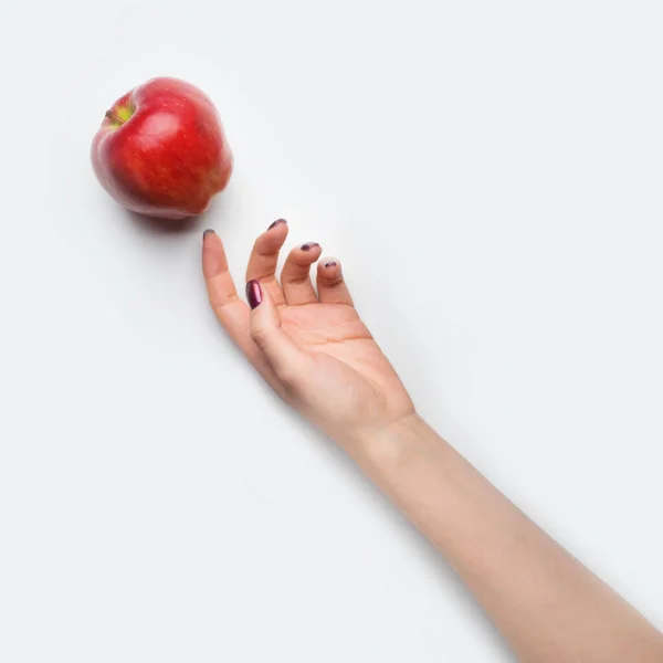 Female hand with red nails dropped red apple on grey background