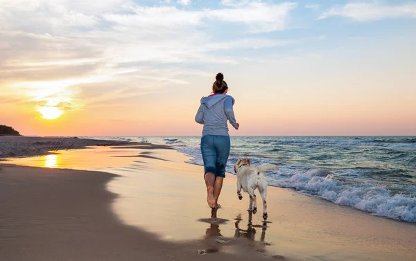A woman running on the beach with a dog — Stock Photo, Image
