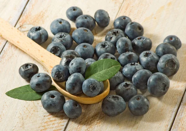 Blueberries in a spoon and scattered on a wooden surface closeup.