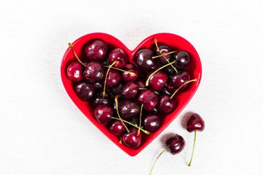 Beyaz ahşap arka planda kalp şeklinde kase kiraz. Seçici odak.