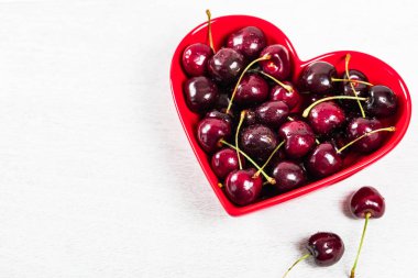 Beyaz ahşap arka planda kalp şeklinde kase kiraz. Seçici odak.