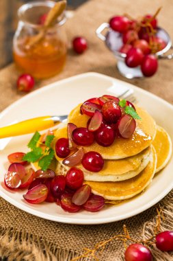 Kahvaltıda dilimlenmiş kırmızı üzüm ve akçaağaç şurubuyla bir yığın krep. Seçici odak.