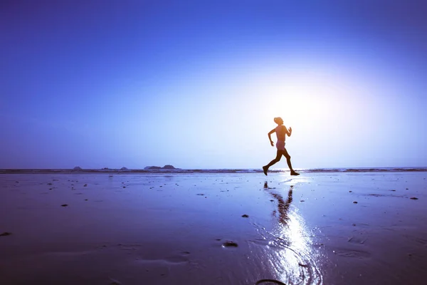 赛跑者剪影在海滩在日落 蓝色背景与复制空间和反射 — 图库照片