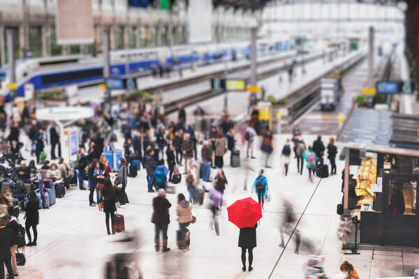 woman with red umbrella waiting at train station and blurred people in motion, solitude concept