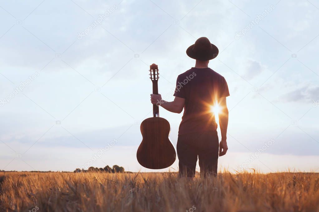 music festival background, silhouette of musician artist with acoustic guitar at sunset fiel