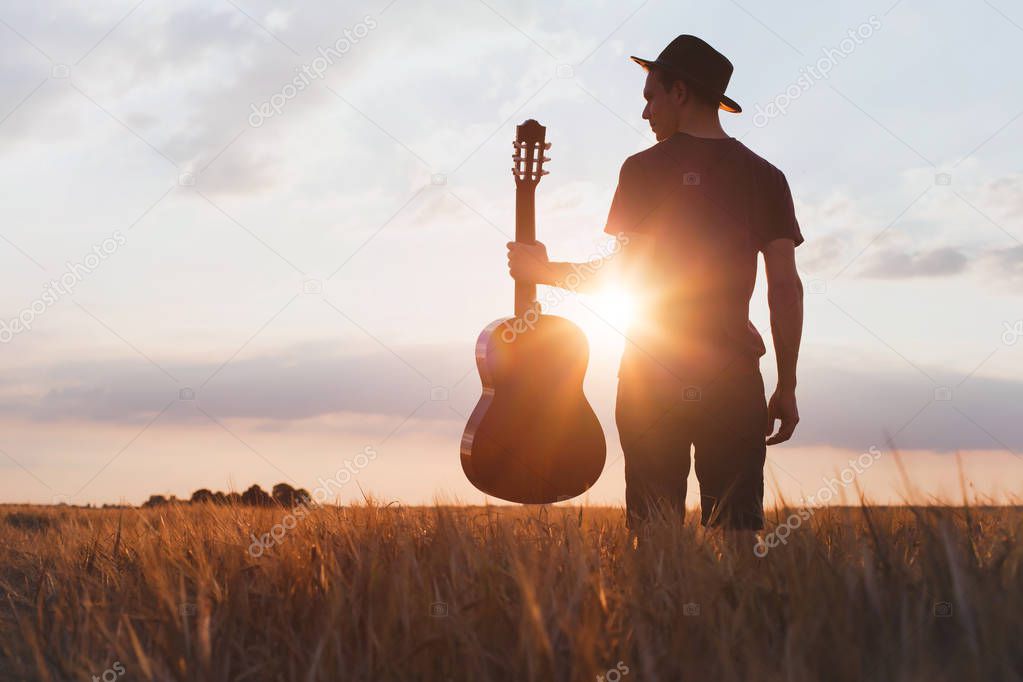 silhouette of musician with guitar at sunset field