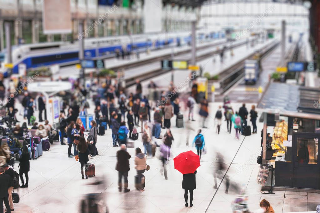 woman with red umbrella waiting at train station and blurred people in motion, solitude concept