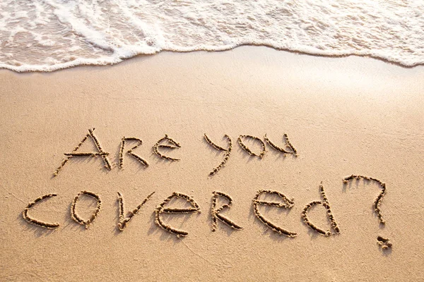 are you covered, travel insurance concept text on the sand beach