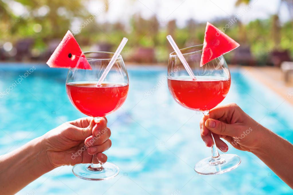 couple drinking cocktails near luxurious swimming pool in hotel, relaxation and tourism, close up of hands with glasses