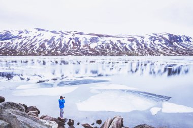 Fotoğrafçı alarak fotoğraf karlı manzara Norveç bahar, dağlarda güzel donmuş göl yakınındaki kişi seyahat