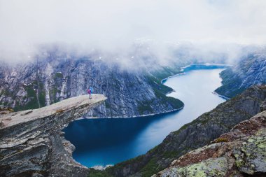 Bulutlu kötü hava, uçurumun üzerinde duran ve fiyort moody gökyüzü ile seyir uzun yürüyüşe çıkan kimse turist backpacker Norveç'te Trolltunga zam
