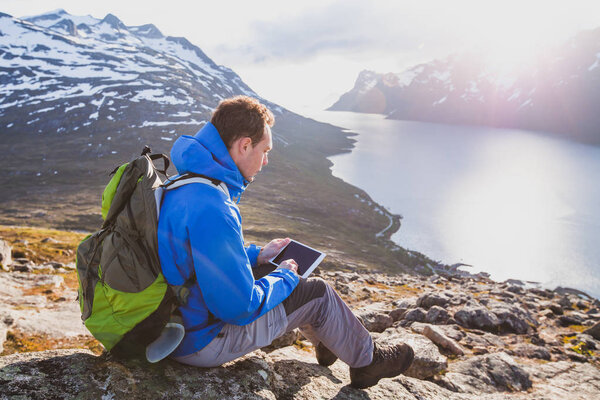 man tourist backpacker using internet application on tablet computer outside in mountains