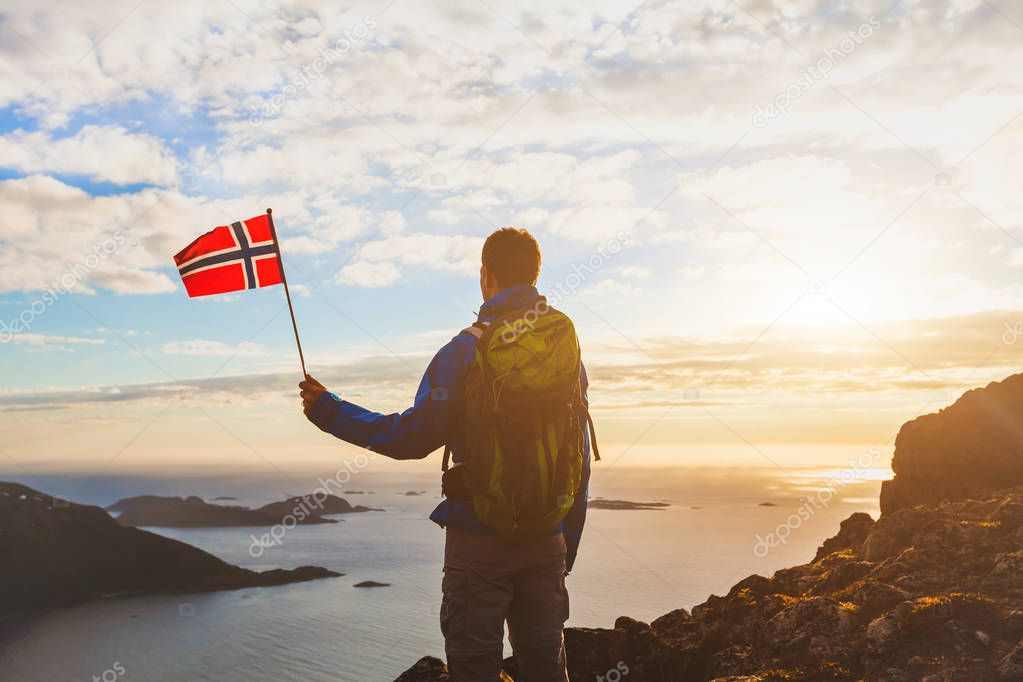 hiking in Norway, silhouette of tourist with norwegian flag looking at beautiful fjord nature with light of midnight sun