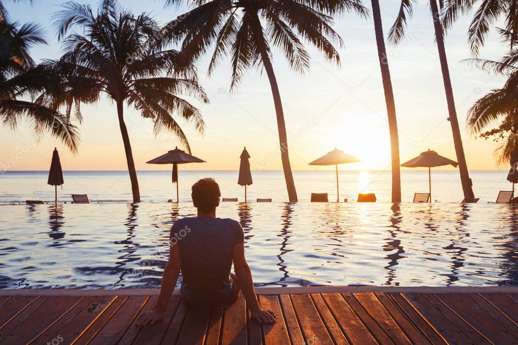 relaxation on the beach, young man enjoying beautiful sunset in luxury hotel near swimming pool