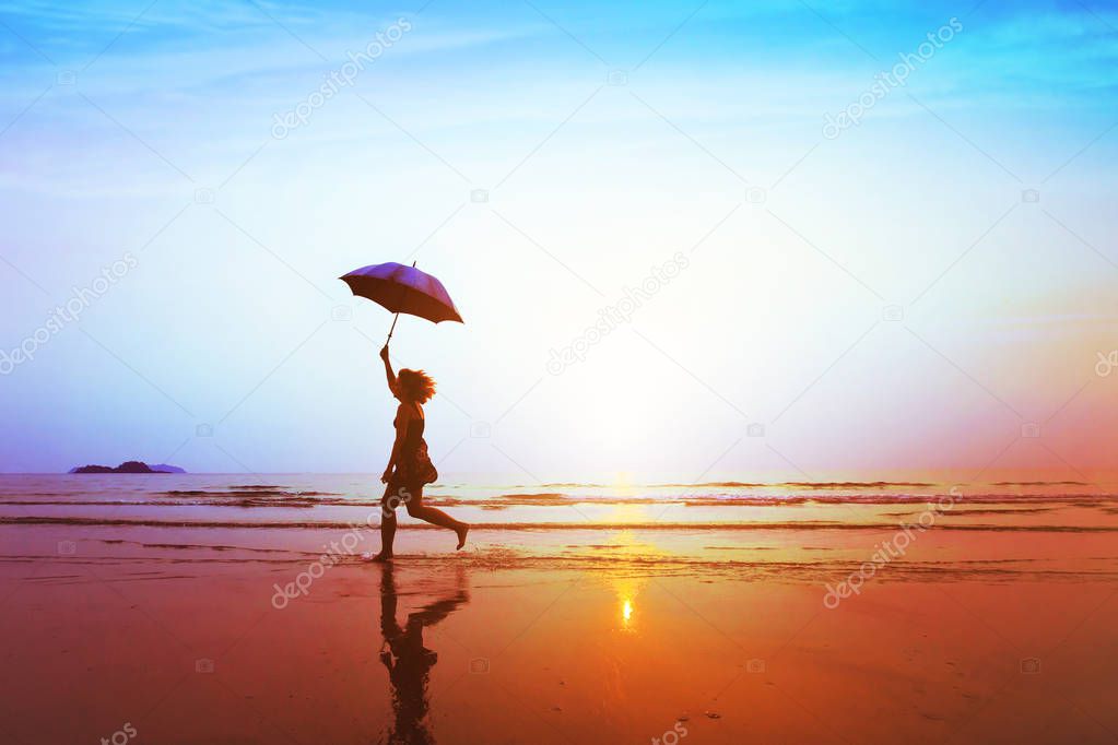 silhouette of happy carefree girl with umbrella jumping on the beach at sunset, freedom and joy concept