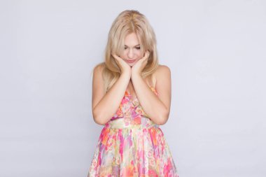 çiçekli pembe elbiseli duygular gösterilen gri arka plan üzerinde genç sarışın bir kadın portresi