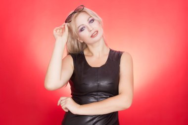 Şık sarışın kadın siyah deri elbiseli ve başında güneş gözlüklü. Sonbahar stil kırmızı zemin üzerine