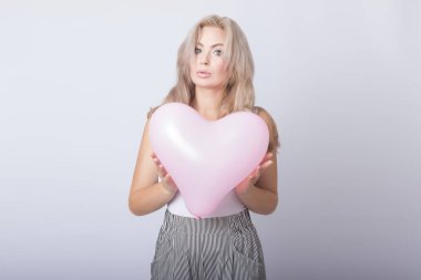 Pembe kalp balon içinde tutan mutlu güzel sarışın kadın gri arka plan üzerinde eller