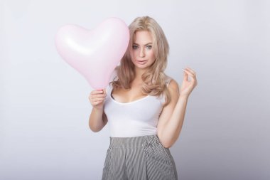 Pembe kalp balon içinde tutan mutlu güzel sarışın kadın gri arka plan üzerinde eller