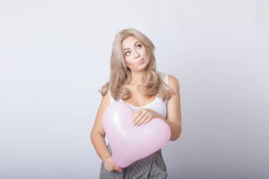Pembe kalp balon içinde tutan mutlu güzel sarışın kadın gri arka plan üzerinde eller