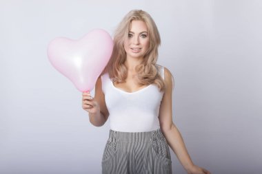 Pembe kalp balon içinde tutan mutlu güzel sarışın kadın gri arka plan üzerinde eller