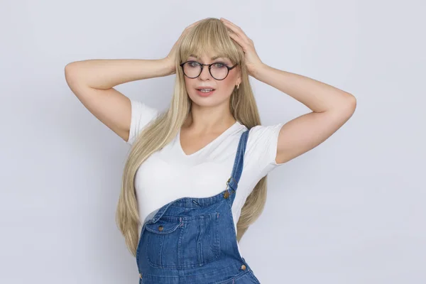 Beautiful blond longhaired woman in jeans overalls and glasses over grey background