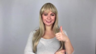 Güzel sarışın kadın gösteren büyük parmak için kamera Studio gri arka plan üzerine