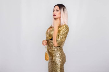 Zarif altın gece elbisesi giyen ve elinde altın renk debriyaj tutan Büyüleyici genç sarı saçlı kadın