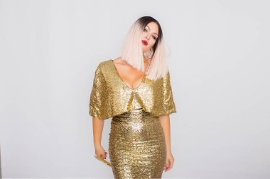 Zarif altın gece elbisesi giyen ve elinde altın renk debriyaj tutan Büyüleyici genç sarı saçlı kadın