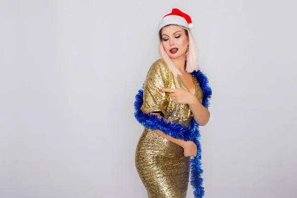 Ενθουσιασμένος νεαρή ξανθιά γυναίκα μαλλιά φορώντας καπέλο Χριστουγέννων και χρυσό φωτεινό φόρεμα — Φωτογραφία Αρχείου