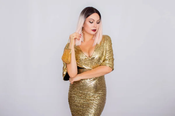 Affascinante giovane donna dai capelli biondi che indossa un elegante abito da sera in oro e tiene in mano la pochette color oro — Foto Stock