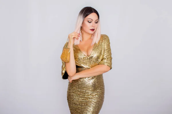 Charmante junge blondhaarige Frau trägt elegantes goldenes Abendkleid und hält goldfarbene Clutch in ihren Händen — Stockfoto