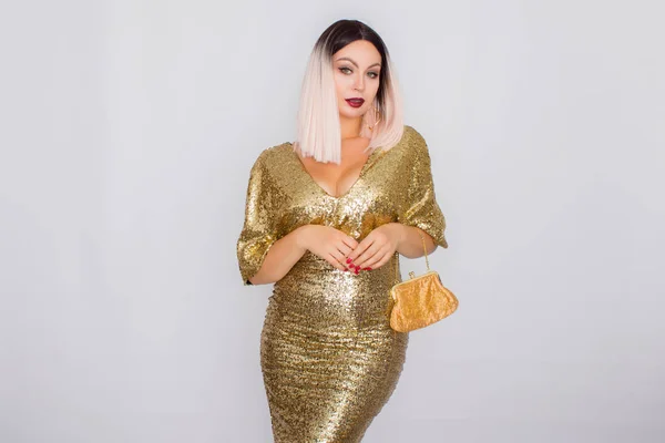 Encantadora mujer de pelo rubio joven con elegante vestido de noche de oro y la celebración de embrague de color oro en sus manos —  Fotos de Stock
