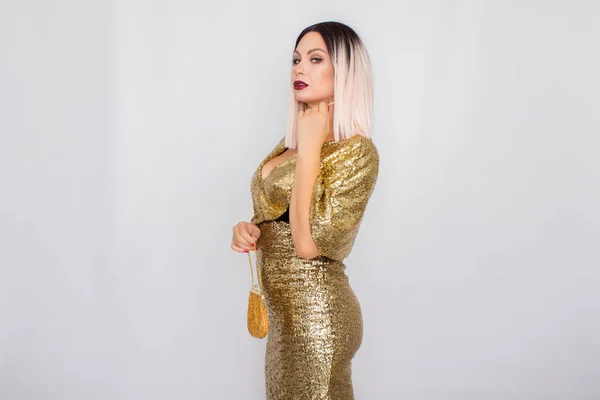 Encantadora mujer de pelo rubio joven con elegante vestido de noche de oro y la celebración de embrague de color oro en sus manos —  Fotos de Stock
