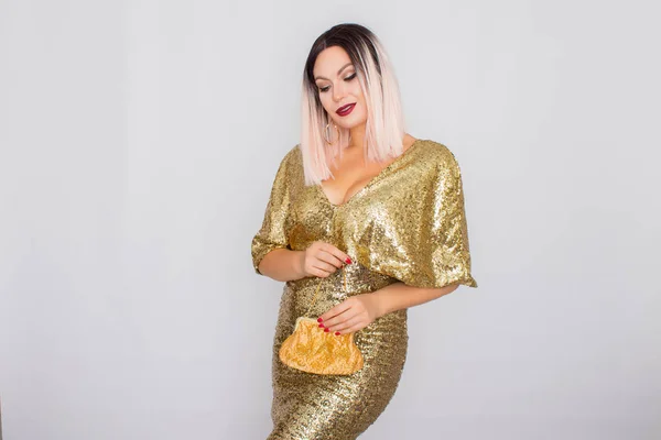 Encantador jovem loira cabelo mulher vestindo elegante vestido de noite de ouro e segurando embreagem cor de ouro em suas mãos — Fotografia de Stock