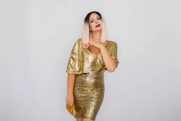 Encantador jovem loira cabelo mulher vestindo elegante vestido de noite de ouro e segurando embreagem cor de ouro em suas mãos — Fotografia de Stock